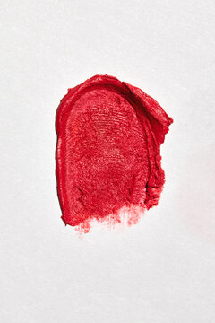 Swatch of red lipstick with fingerprint texture on white background.