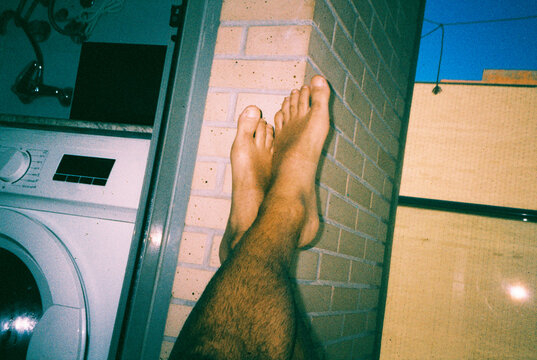 a man resting his bare feet against a brick wall, 35mm film