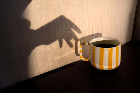 Striped cozy yellow mug with hot drink and hand shadow.