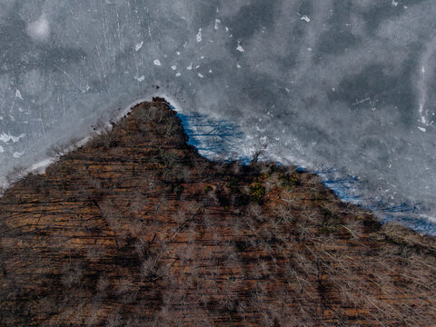 Top view of icy lake beside leafless forest