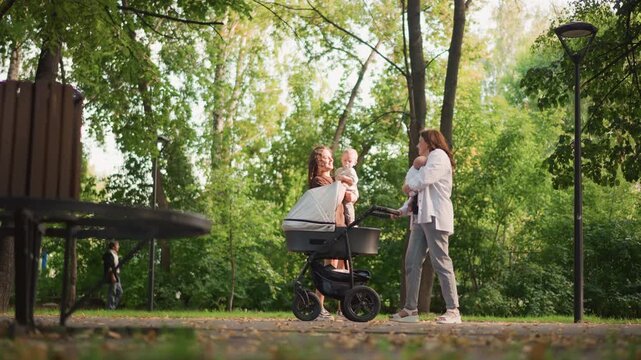 Mothers pause with stroller near bench under dappled trees, gentle baby cuddle and quiet conversation about routine and parenting decree, soft sunlight, reflective mood and supportive community vibe.
