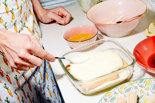 the man smooths the final creamy layer of tiramisu