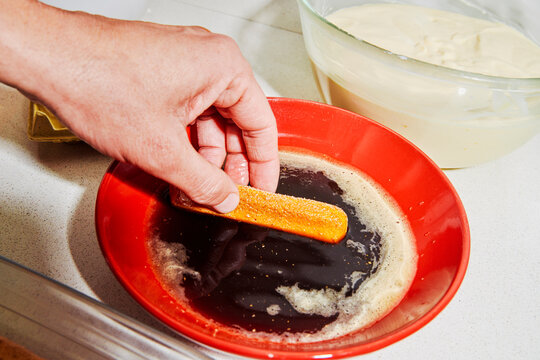 a man dips a ladyfinger in coffee for tiramisu