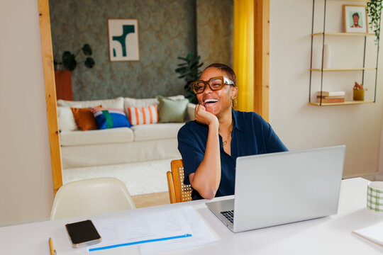 Woman laughing while working on laptop at home