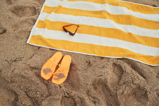Beach sandals and towel on sandy beach