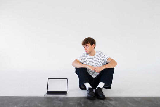 Young Man Sitting With Laptop In Minimal Studio