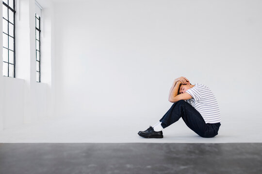 Man Sits on Floor in White Studio, Anxious