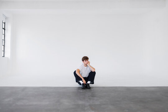 Casual Man Sitting Cross-Legged In White Studio