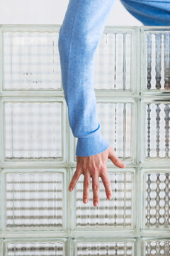 Hand Reaching Through Glass Block Wall in Blue Sweater