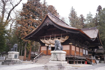 Obraz premium Ancient shrine stands beneath overcast sky. Stone lions guard the entrance with solemn presence. Wooden architecture showcases traditional craftsmanship