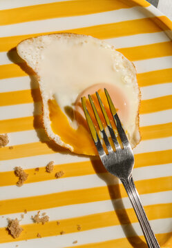 Partially Eaten Fried Egg Close up on Striped Yellow Plate with Fork.