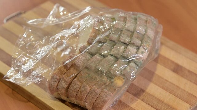 A man puts spoiled white bread in a plastic bag on a wooden board. Man notices green mold on bread, process of blooming and spoiling food, not thrifty, expiration date and loss of quality