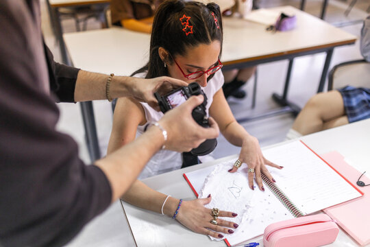 Teacher filming student opening crumpled paper in class