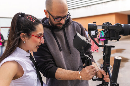 Videographer showing footage on camera screen in school courtyard