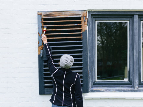 woman painting wooden shutters on a house