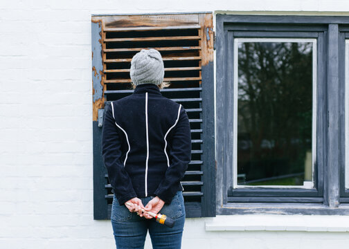 woman painting wooden shutters on a house