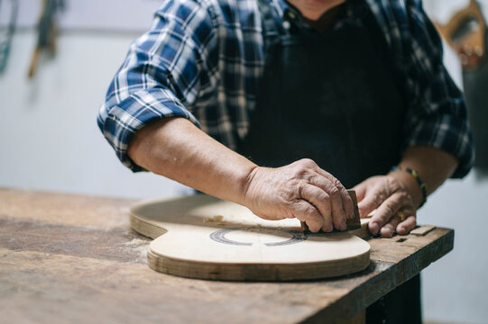 Luthier sanding handmade guitar in workshop, craftsmanship concept