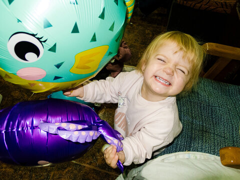 Toddler girl smiling broadly holding party balloons
