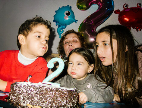 Family celebrating 2nd birthday blowing cake candle