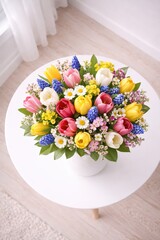 Bunter Fr&uuml;hlingsblumenstrau&szlig; mit Tulpen, Traubenhyazinthen und kleinen Bl&uuml;ten in wei&szlig;er Vase auf rundem wei&szlig;en Tisch.