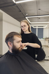 Fototapeta premium Professional woman barber wielding electric hair clipper making Fashionable haircut. Bearded Man client visit gentleman grooming beauty salon for hairstyle care. Modern Haircut style in barber shop