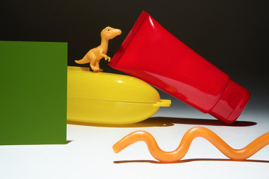 Red hand cream tube and various colorful shapes on dark background.