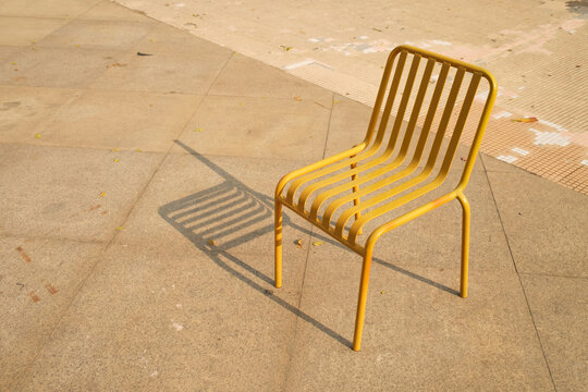 Yellow metal chair on a concrete surface with shadows 