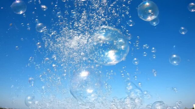 Clear blue sky filled with shimmering soap bubbles and water splashes on a sunny day