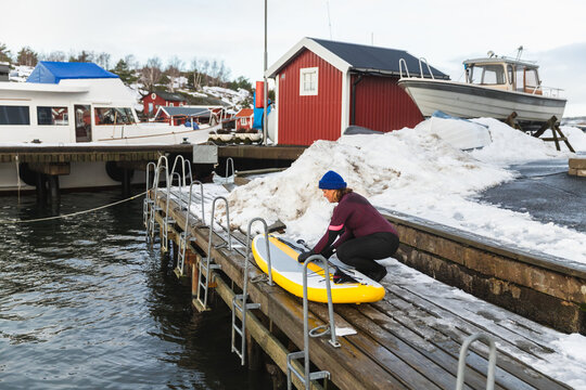Woman Launching Paddleboard into the Water in Snowy Swedish Port