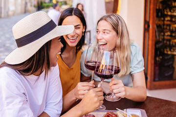 Happy women friends celebrating with red wine at outdoor cafe. Young female friends enjoying joyful social moment in Europe. Lifestyle and social concept. © Xavier Lorenzo