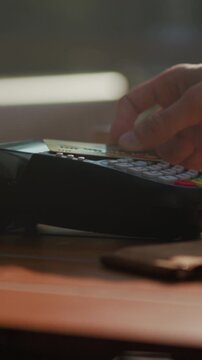 Deposit card into reader amid warm lighting, Cash transaction occurring on wooden surface with soft glow