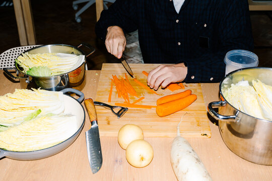 An anonymous man&rsquo;s hands slicing bright orange carrots