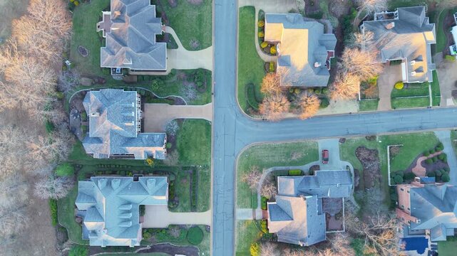 An aerial top-down video of a quiet American suburban street and cul-de-sac, featuring upper middle-class residential homes, manicured lawns, and property landscaping.
