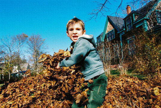 Playful Child Winds Up to Throw Autumn Leaves at Parent