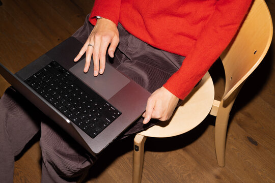 Person using laptop on wooden chair indoors
