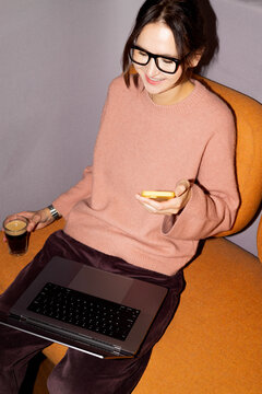 Businesswoman multitasking with smartphone and laptop indoors