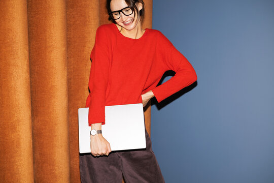 Woman holding laptop in business casual outfit indoors