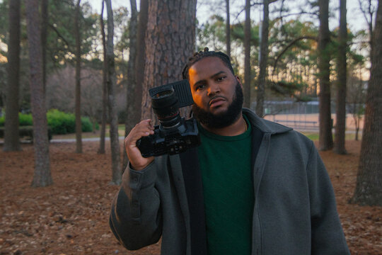 Man Holds Camera in Forest During Evening Hour in Park Setting