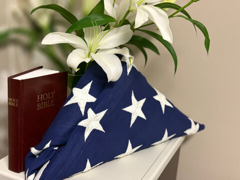 Folded American Flag with Holy Bible and White Lilies, Veteran Memorial and End of Life Remembrance Concept
