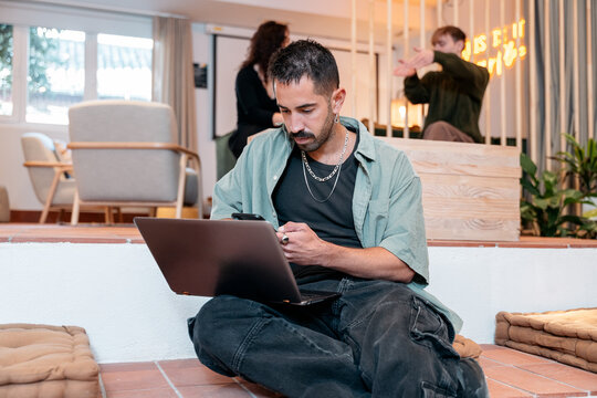 Millennial man multitasking with laptop and smartphone in coliving