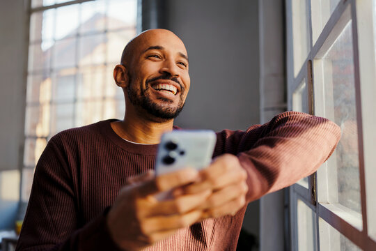 Happy man using smartphone feeling joy by window