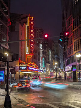 Vibrant night time Boston Massachusetts street scene featuring illuminated Paramount Theater neon sign with reflections and long‑exposure urban city lights