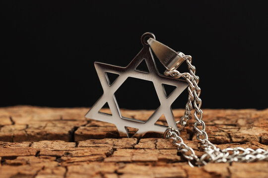 Holocaust Remembrance Day. Pendant in shape of Star of David and metal chain on wooden surface against black background, closeup