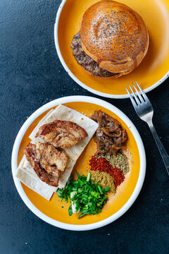 Grilled meat with spices and hamburger bun on yellow plates