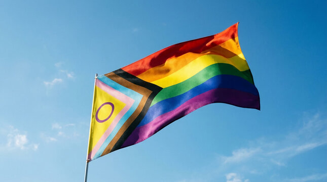 Bright rainbow flag against the blue sky, the flag is wavy and includes diverse stripe and symbol, representing inclusivity and community value