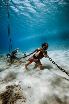 boy pulling heavy chain along sandy seabed
