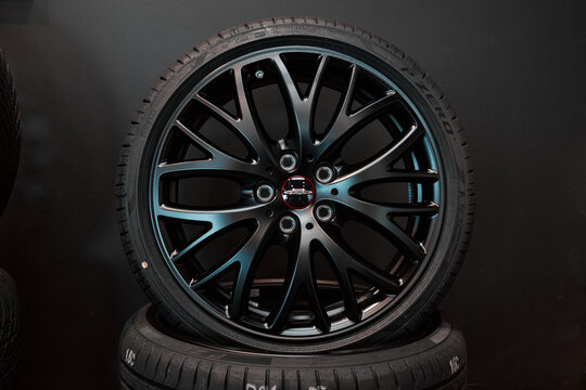 A black car wheel with a tire rests on top of another tire. The wheel shows a decorative design. A dark background makes the wheel stand out. 04.05.2023- Katowice, Poland