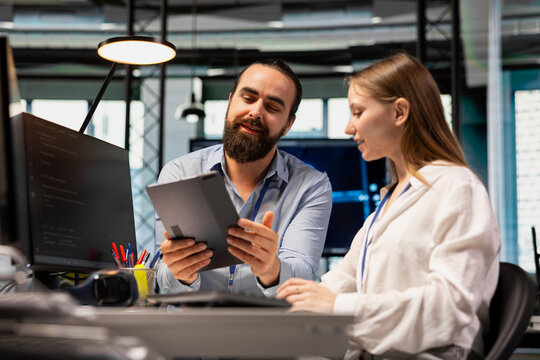 Lead technician providing support to new employee in software development agency using tablet. Seasoned IT expert using device to present best practices to trainee during internship in tech startup