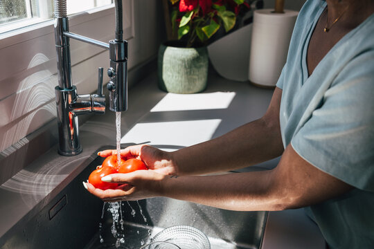 Person washing tomatoes under kitchen faucet