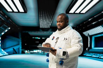 Fototapeta premium Cosmonaut in starship navigating orbital trajectory using tablet, doing galaxy expedition for future of mankind. African american astronaut mapping unknown worlds, exploring planets